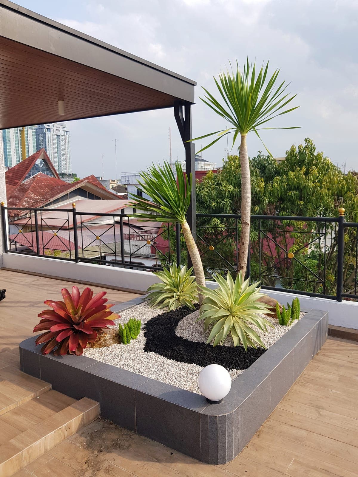 Taman rooftop dengan tanaman palem dan bromelia merah di atas batu putih